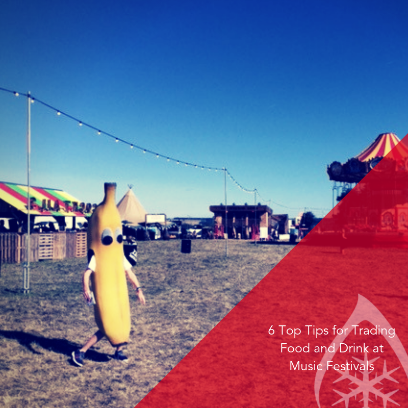 A person in a large banana costume walks across a grassy area at a festival.