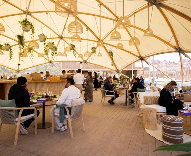 Brightly lit indoor dining space with natural textures, featuring plants and patrons enjoying meals.