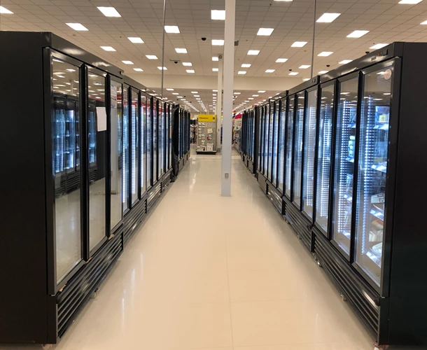 Aisle of glass-fronted fridges with black frames, reflecting bright overhead lights in a retail space.
