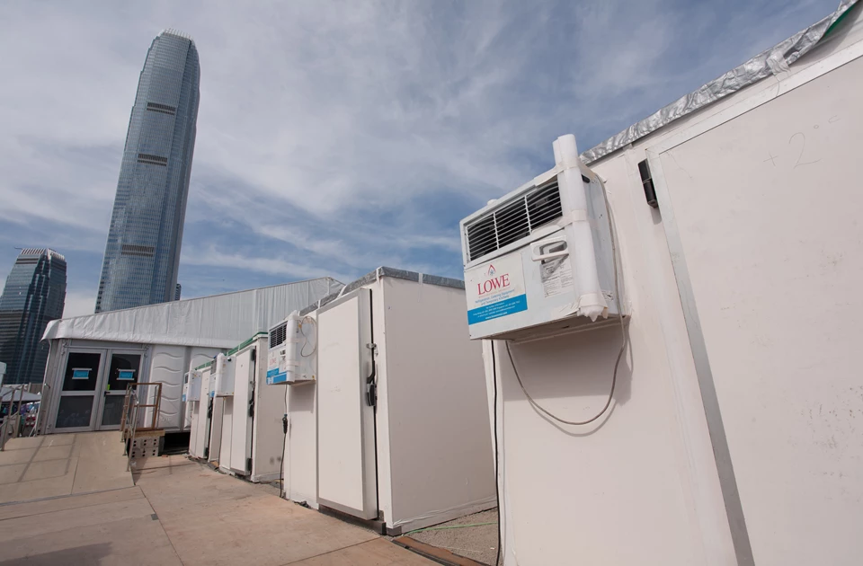 White storage units lined up under a blue sky, with a tall building visible in the background.
