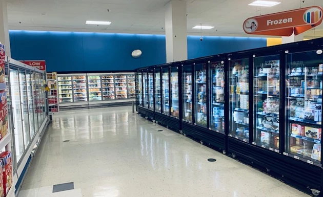 Supermarket aisle featuring glass-fronted freezers against a blue wall and shiny white floor.