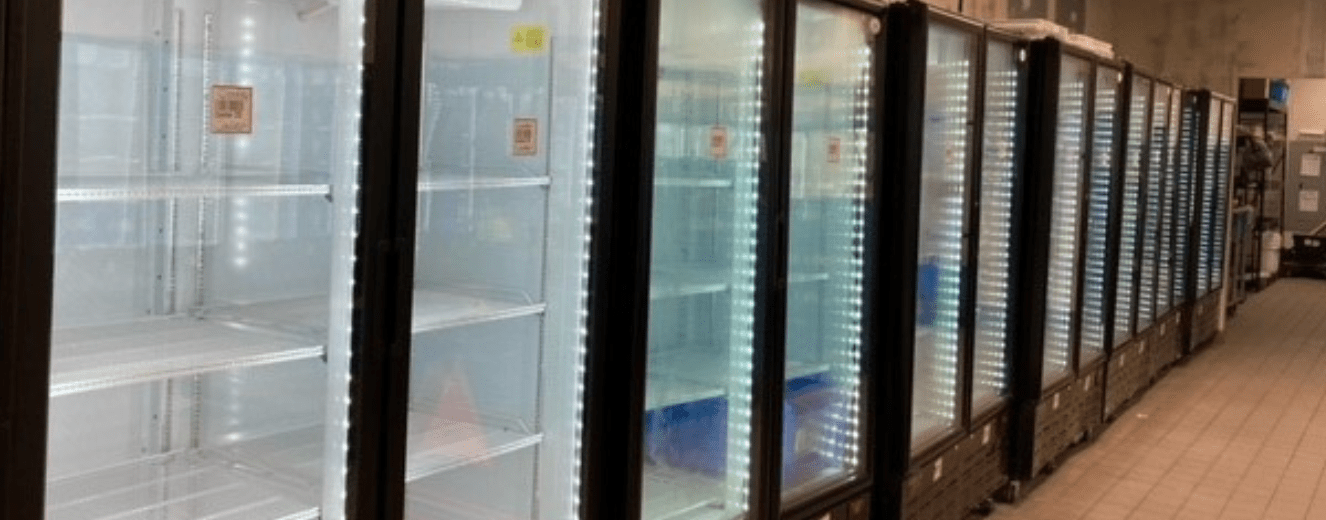 Empty glass-fronted refrigeration units with bright white lighting in a retail environment.
