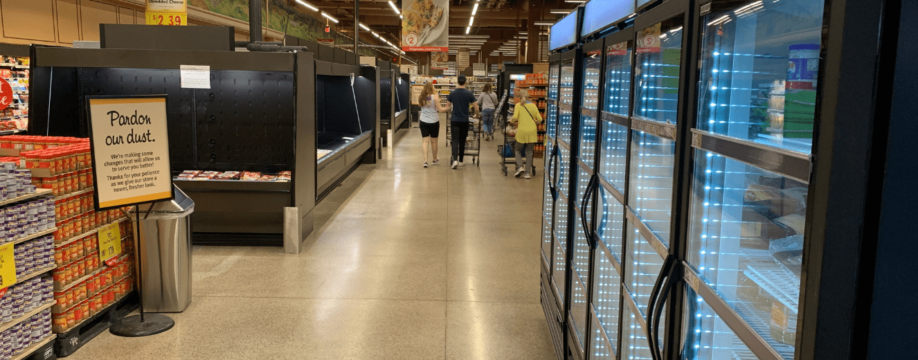 Shoppers navigate a grocery aisle with dairy cases, featuring bright blue and silver refrigeration units.
