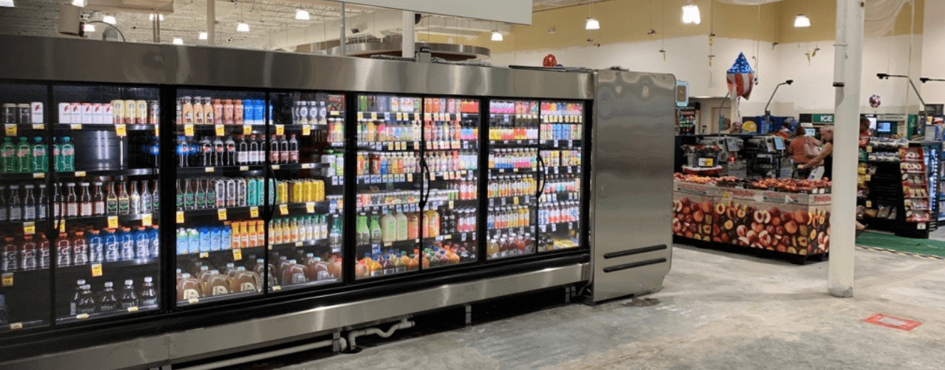 Brightly lit beverage fridge displaying a variety of colourful drinks against a sleek metallic background.