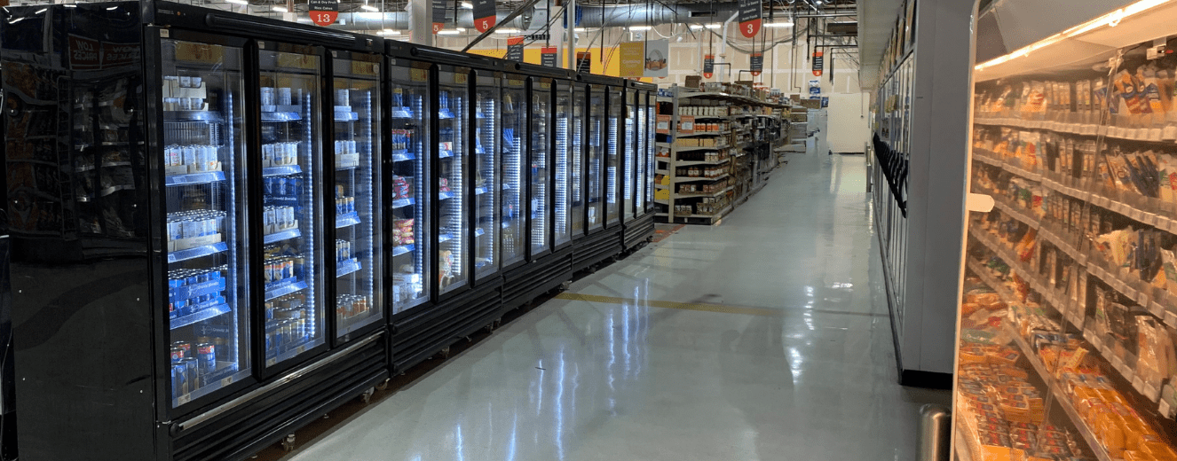Refrigerated display cases line a brightly lit aisle with polished grey flooring in a retail environment.