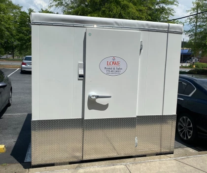 White storage unit with a silver base, parked outside a restaurant, surrounded by vehicles.