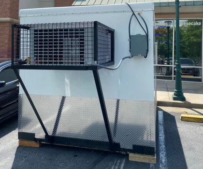 Large white emergency cooling unit with a black metal frame, positioned on a concrete surface.