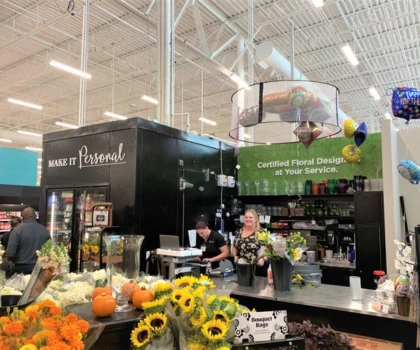 Brightly coloured flowers and produce displayed at a market stall with a black counter and green signage.