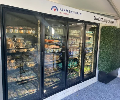 Refrigerated display unit filled with various packaged foods, featuring a black exterior and bright signage.