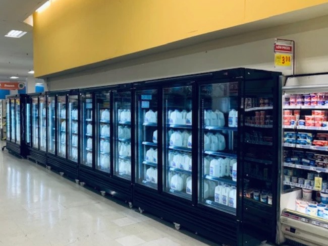 Black glass refrigerator units displaying various packaged items under bright lighting in a retail space.