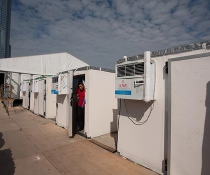 White portable units lined up outdoors, with a person in a red shirt standing by one.
