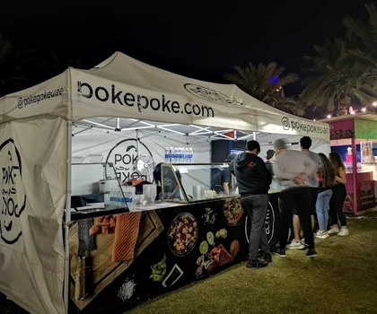 A food stall with a white canopy and colourful graphics, serving customers at night.