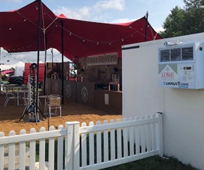 Red canopy covering a wooden event space, with a white fence and signage visible.