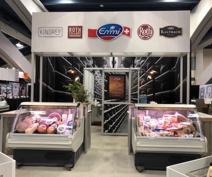 Exhibition stand featuring refrigerated displays of meat products, with a white and black backdrop.
