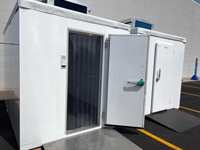 White outdoor cold rooms with metal doors, featuring a grey entrance and clear plastic strip curtain.