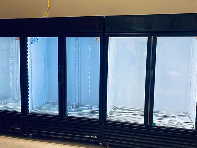 Three black commercial refrigerators with glass doors, empty interiors, and blue lighting inside.