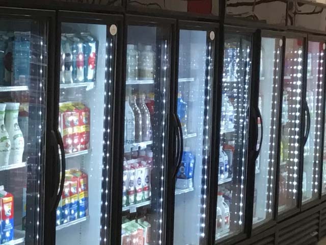 Six glass-fronted vending machines displaying various beverages, illuminated with bright LED lights.