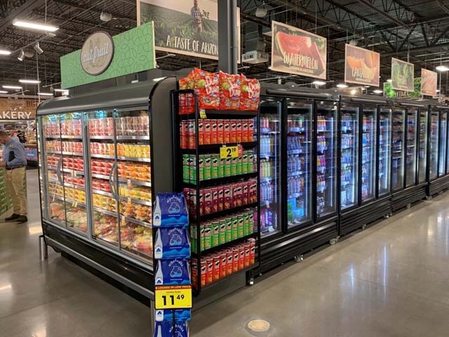 A supermarket aisle featuring colourful frozen food displays and beverage shelves, with bright signage.