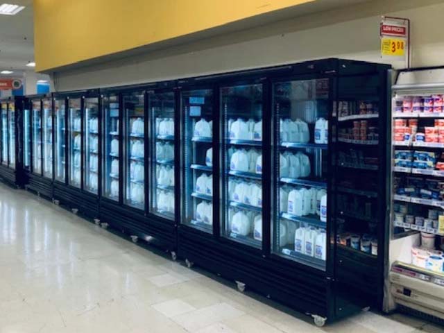 A row of glass-fronted refrigerators displaying various white products against a yellow wall.