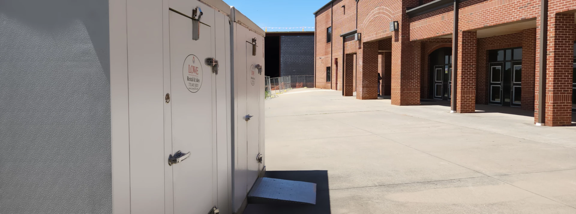 White storage units in a paved area, with red brick buildings and clear blue sky in the background.