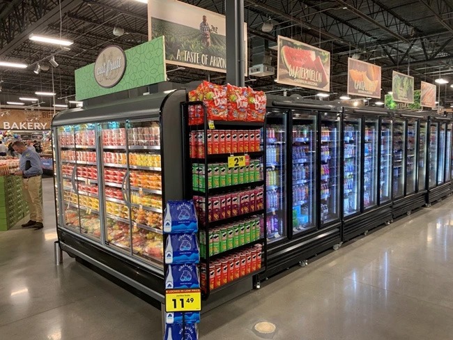 Grocery store aisle featuring black freezer units filled with colourful products and illuminated signage.