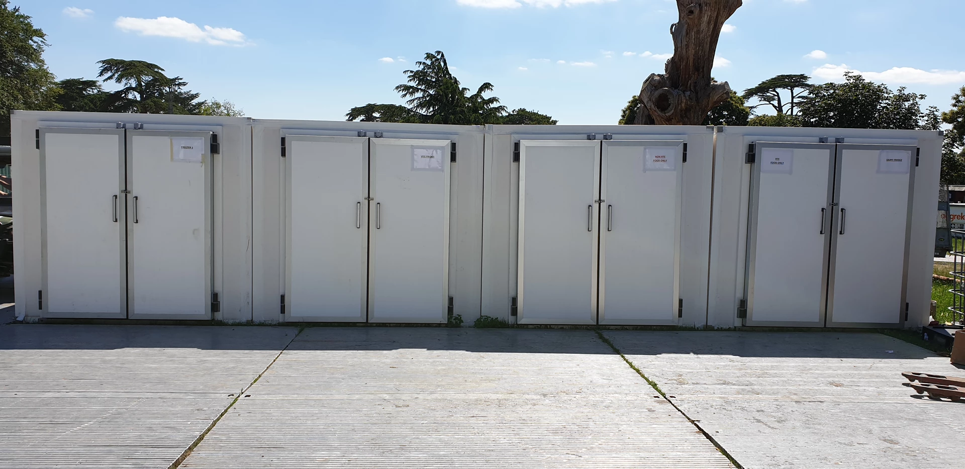 Four white walk-in coolers and freezers lined up against a clear blue sky.