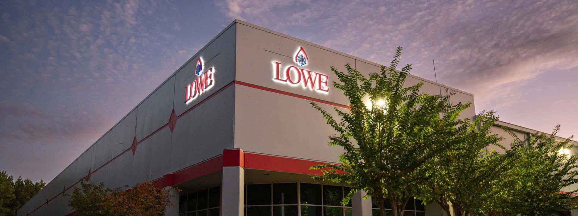 Lowe's store exterior with grey walls, red accents, and illuminated signage against a twilight sky.