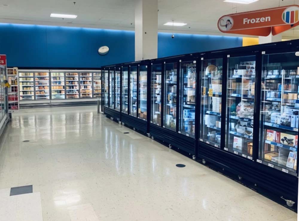Rows of glass-fronted freezers with a blue wall background in a retail environment.