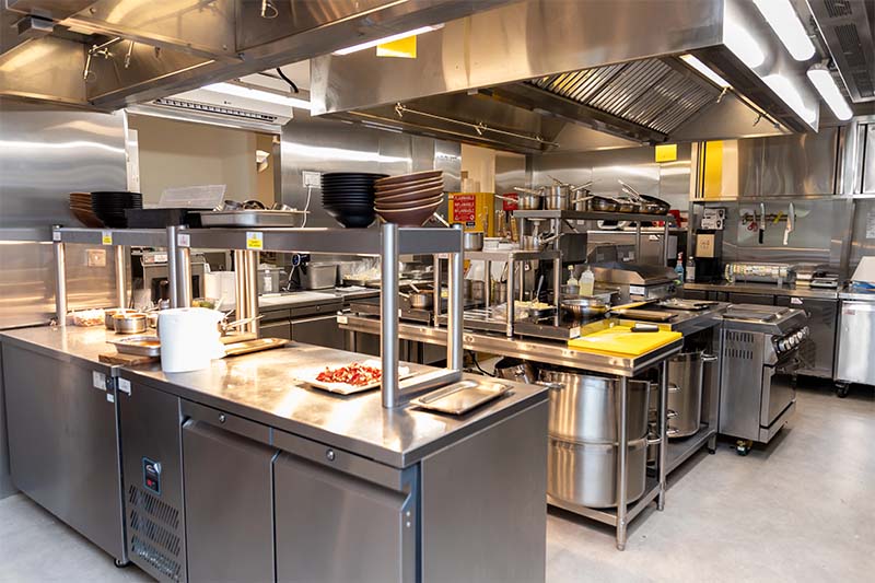 Modern stainless steel kitchen with various cooking equipment and utensils, featuring yellow accents.