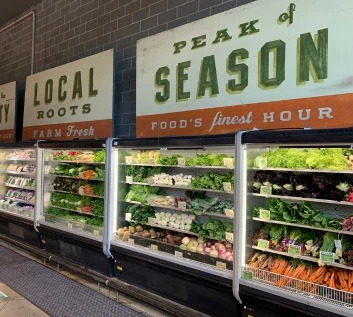 Fresh produce displayed in vibrant greens and oranges, with signage reading 