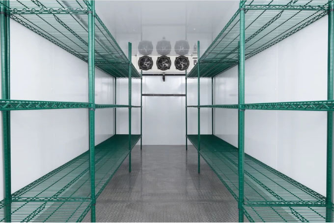 Walk-in cooler interior featuring green metal shelving and ceiling-mounted cooling units in a white environment.