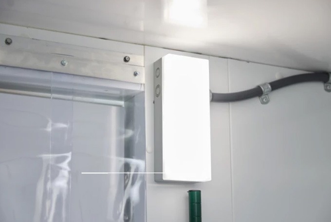 Bright white LED light fixture mounted inside a walk-in cooler, with grey pipe visible in background.