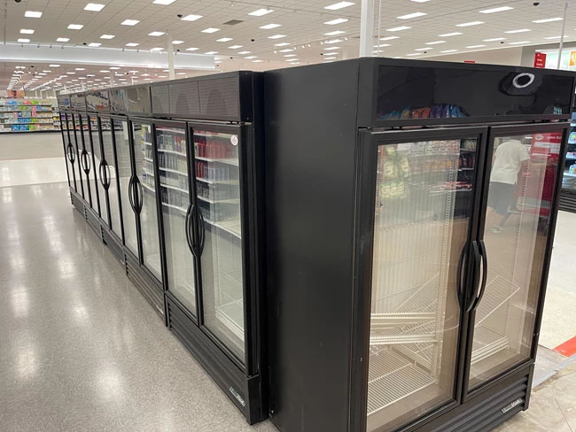 Black refrigerated display units in a retail space, featuring glass doors and bright overhead lighting.